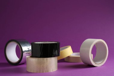 Mor arka planda farklı yapışkan bantların ruloları