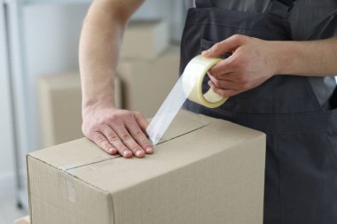 Kapalı alanda yapıştırıcı bantlı karton kutu mühürleyen adam.