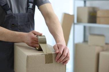 Kapalı alanda yapıştırıcı bantlı karton kutu mühürleyen adam.