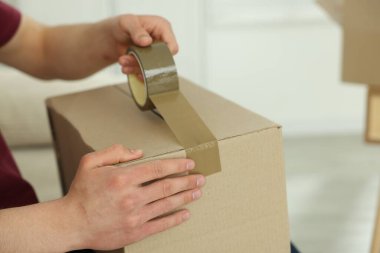 Kapalı alanda yapıştırıcı bantlı karton kutu mühürleyen adam.