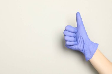 Tıbbi eldivenli doktor açık gri arka planda baş parmak gösteriyor, yakın plan. Metin için boşluk