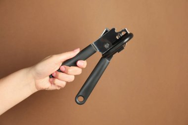 Kadın konserve açacağını kahverengi arka planda tutuyor, yakın plan.