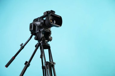Açık mavi arkaplanda tripodu olan modern video kamera, metin için boşluk