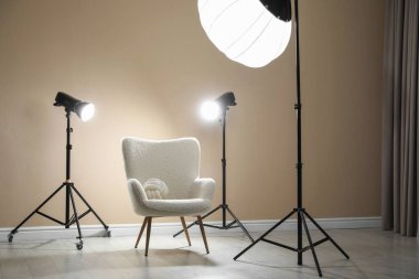 Profesyonel ışıklandırma ekipmanları ve fotoğraf stüdyosunda dekoratif yastıklı koltuk.