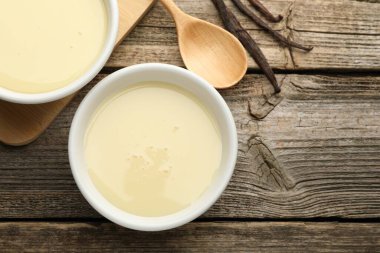 Yoğunlaştırılmış süt, kaşık ve vanilya kapsülleri ahşap masada, düz yerde. Metin için boşluk