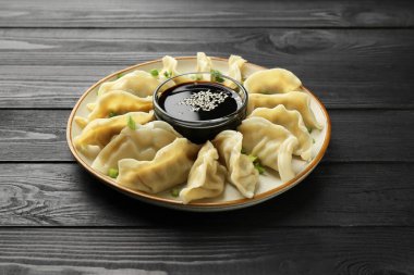 Lezzetli haşlanmış gyoza (hamur tatlısı) yeşil soğan ve soya sosu siyah ahşap masada.