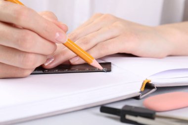 Beyaz masadaki deftere cetvel ve kalemle çizim yapan kadın, yakın plan.