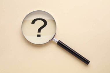 Bej arkaplanda soru işareti, büyüteçle üstten görünüm