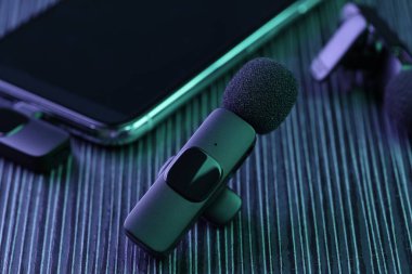 Lavalier mikrofon ve kablosuz alıcısı olan akıllı telefon. Karanlık ahşap masa, neon ışıklar, yakın plan.