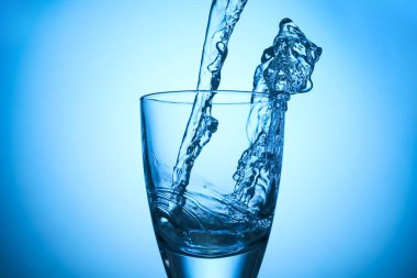 Pouring refreshing soda water into glass on light blue background, closeup