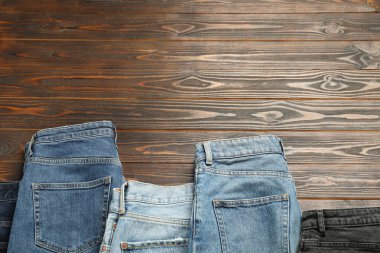 Different stylish jeans on wooden background, flat lay. Space for text