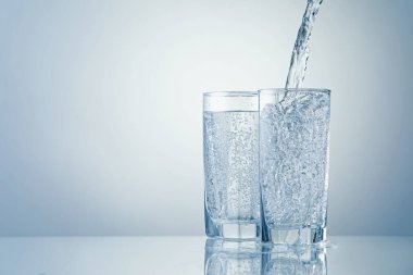 Açık gri arka planda bardaklara ferahlatıcı soda dökülüyor, yakın plan. Metin için boşluk