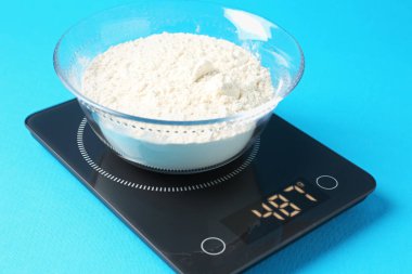 Açık mavi zemin üzerinde un bulunan elektronik mutfak terazisi, yakın plan.