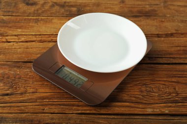 Modern electronic kitchen scale with plate on wooden table, closeup