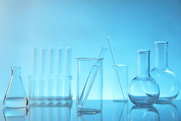 Laboratory glassware on mirror surface against light blue background