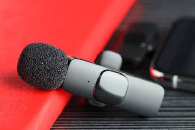 Lavalier mikrofon, kablosuz alıcısı olan akıllı telefon ve siyah ahşap masada kırmızı defter, yakın plan.