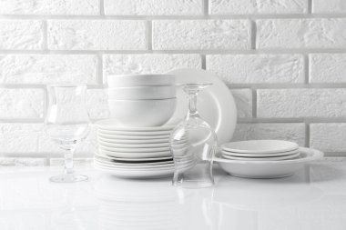 Different clean dishware on white table near brick wall