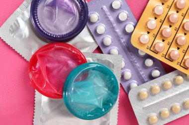 Pembe arka planda doğum kontrol hapı ve prezervatif kabarcıkları var.