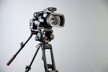 Açık gri arkaplanda tripodu olan modern video kamera, metin için boşluk