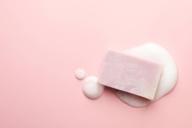 Açık pembe arka planda köpüklü sabun çubuğu, üst manzara. Metin için boşluk