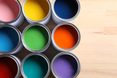 Cans of bright paints on wooden table, flat lay. Space for text