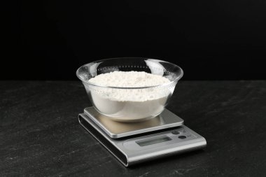 Elektronik mutfak terazisi ve siyah arka planda koyu dokulu bir kase un.