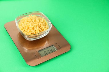 Elektronik mutfak terazisi ve yeşil arka planda bir kase çiğ makarna. Yakın plan. Metin için boşluk