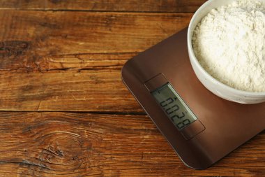 Modern electronic kitchen scale with bowl of flour on wooden table, closeup. Space for text