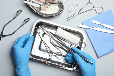 Gri arka planda farklı cerrahi aletlere sahip doktor, üst görünüm