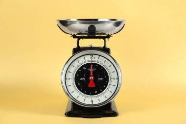 Mutfak terazisinde sarı arka planda kâse var.