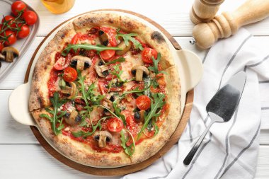 Mantarlı, domatesli, roka ve beyaz ahşap masada servis edilen lezzetli bir pizza.