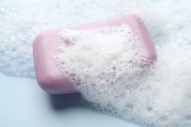 Açık mavi arkaplanda köpük olan sabun çubuğu, yakın plan