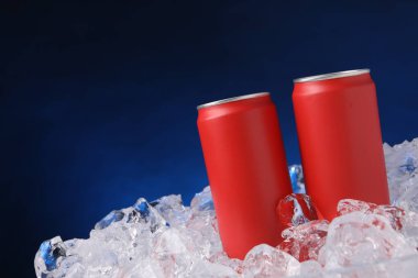 Refreshing drinks in cans on ice cubes against dark blue background