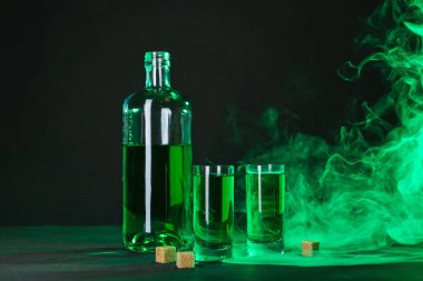 Absinthe shot bardakları, şişe ve esmer şeker siyah arka planda dumanlı