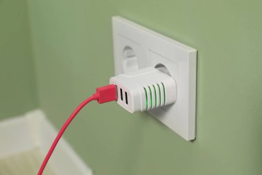 Açık yeşil duvardaki elektrik prizine bağlı USB adaptörüName