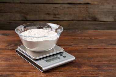 Elektronik mutfak terazisi ve ahşap masa üzerinde bir kase un. Metin için boşluk