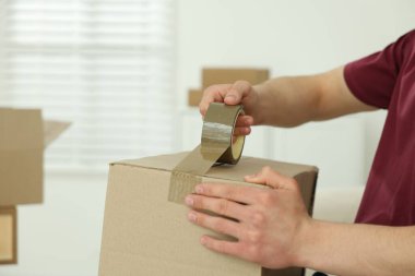 Kapalı alanda yapıştırıcı bantlı karton kutu mühürleyen adam.