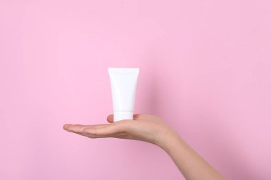 Pembe arka planda krem tübü olan kadın, yakın plan. Vücut bakımı ürünü