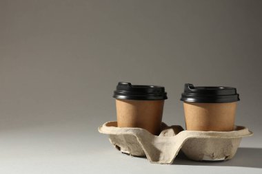 Paper coffee cups in cardboard holder on light grey background. Space for text