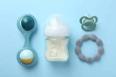 Sütlü beslenme şişesi, bebek çıngırağı, açık mavi arka planda ip ve emzik, düz uzanma