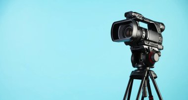 Açık mavi arkaplanda tripodu olan modern video kamera, metin için boşluk