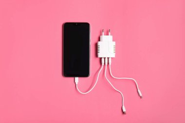 USB şarj kablosu pembe arka plandaki akıllı telefona bağlı, üst görünüm