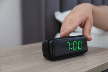 Kapalı bir odada, komodinin üzerindeki dijital çalar saati kapatan adam.