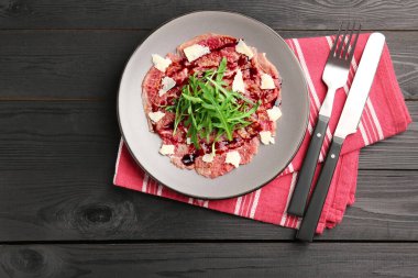 Fresh beef carpaccio with arugula, cheese and sauce on black wooden table, top view