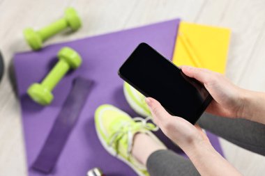 Akıllı telefonu ve spor aletleri olan bir kadın evin içinde, manzaranın üstünde.