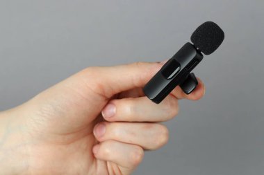 Açık gri arkaplanda lavalier mikrofon tutan kadın, yakın plan.