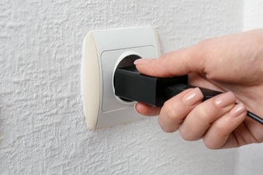 Kadın USB güç adaptörünü şarj kablosuyla kapalı mekandaki elektrik prizine takıyor.