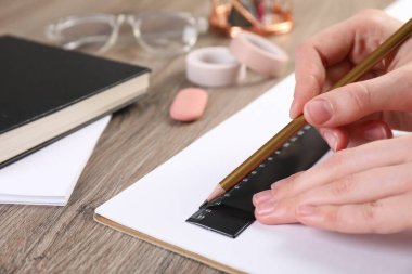 Ahşap masada cetvel ve kalemle çizim yapan kadın, yakın plan.