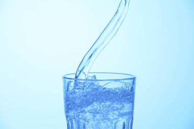 Açık mavi arkaplanda bardağa soda dökülüyor, yakın plan.