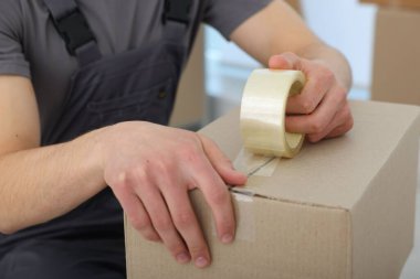 Kapalı alanda yapıştırıcı bantlı karton kutu mühürleyen adam.